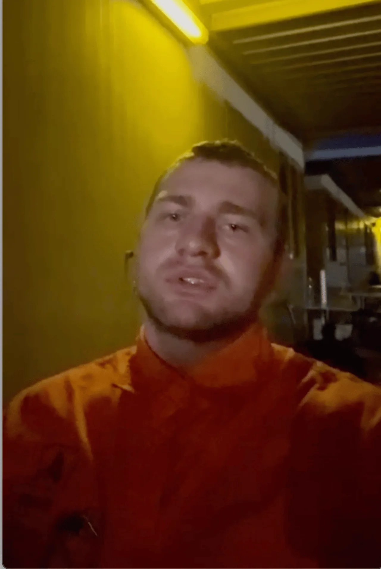 David F. in orangefarbenem Arbeitshemd in einem beleuchteten Werkstattgang