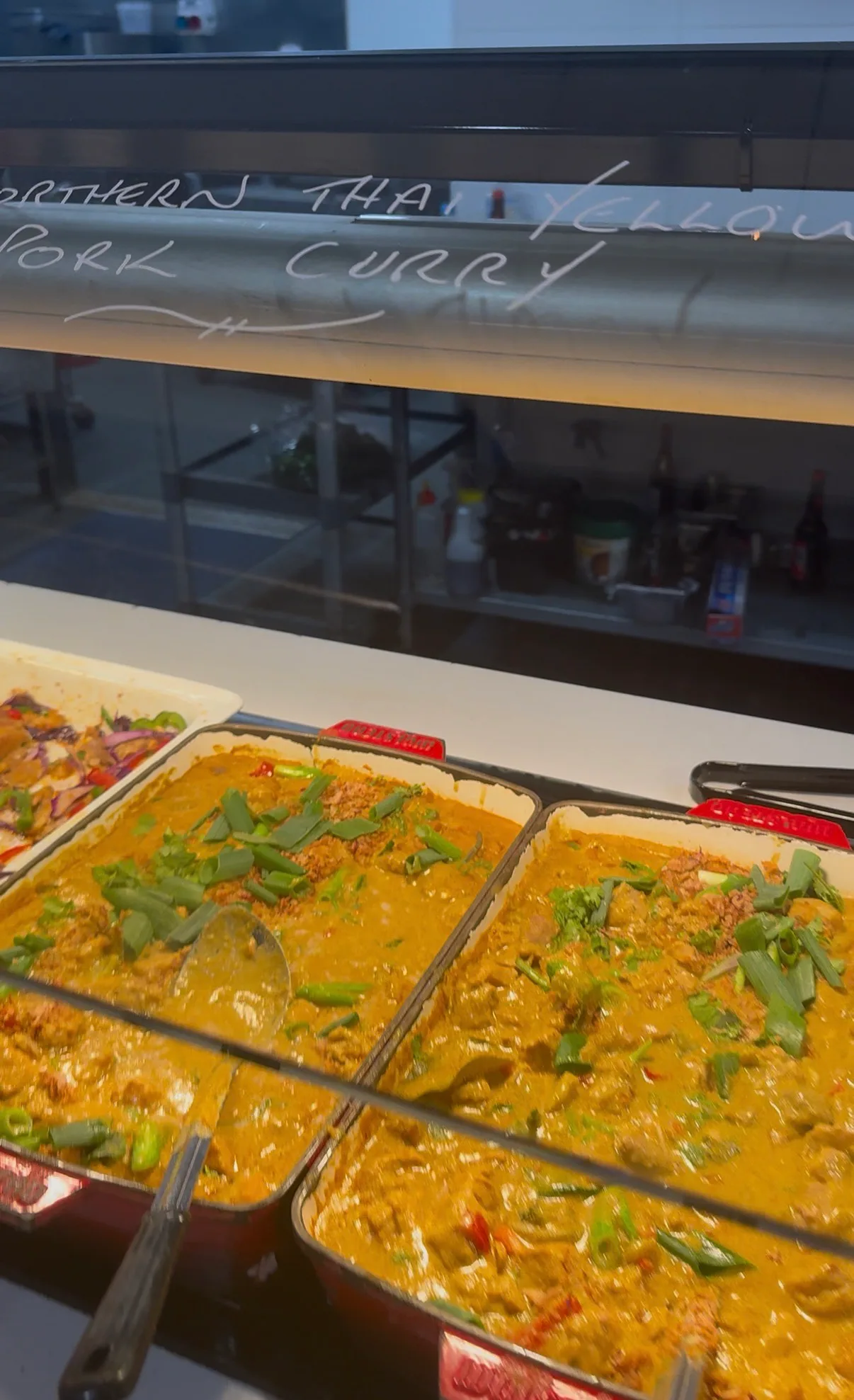 Zwei große Behälter mit Thai Yellow Pork Curry in der Buffetauslage, darüber die handgeschriebene Tafel mit dem Gerichtnamen