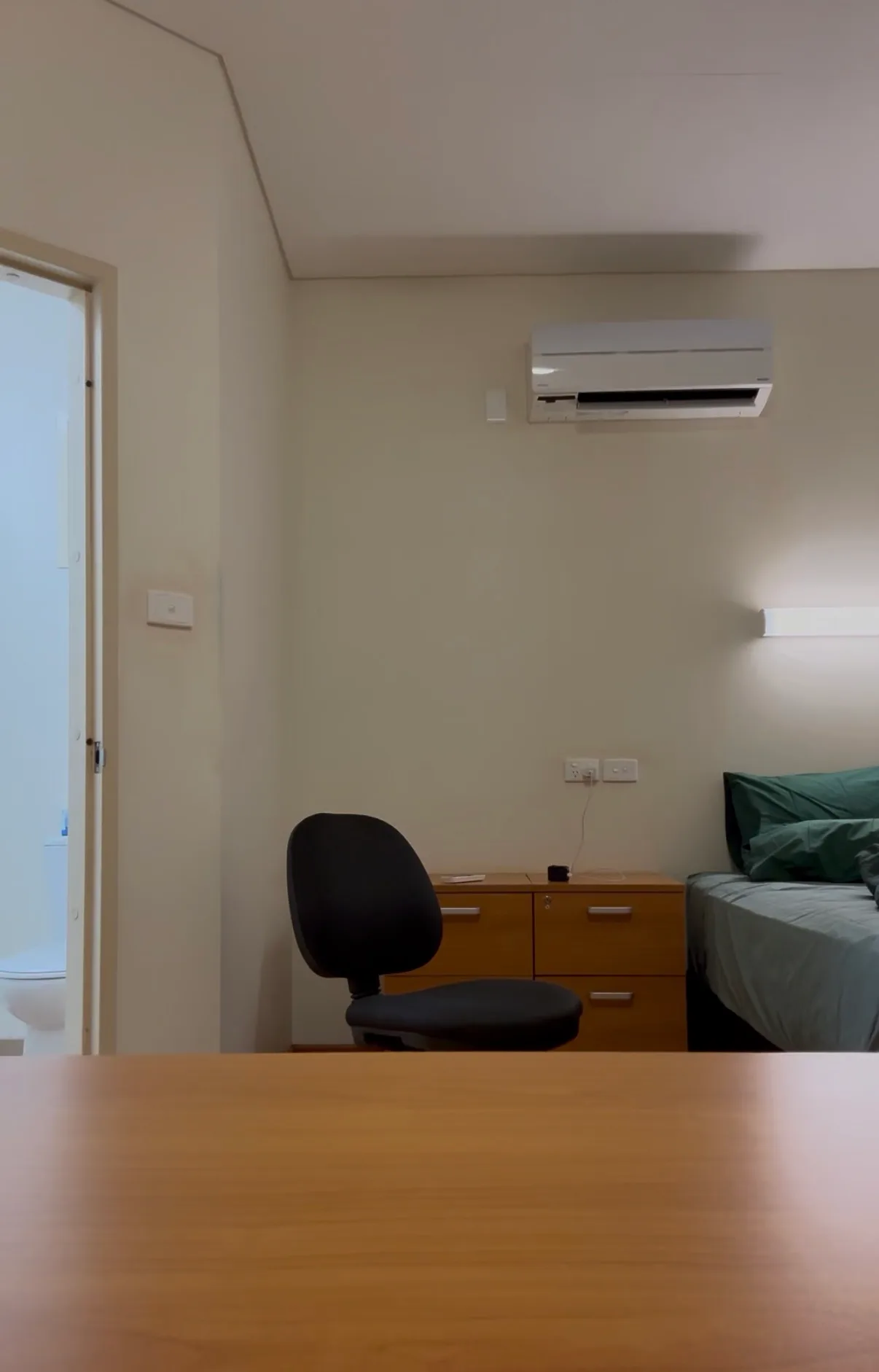 Zimmer in einem Donga mit Einzelbett, Schreibtisch, Bürostuhl, Klimaanlage und offener Tür zum eigenen Bad