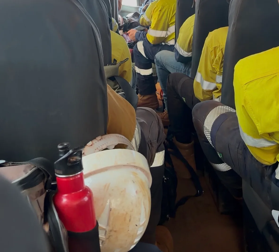 Blick durch den Mittelgang eines vollen Crew Bus auf Bergarbeiter in gelben Warnhemden auf dem Weg zur Schicht