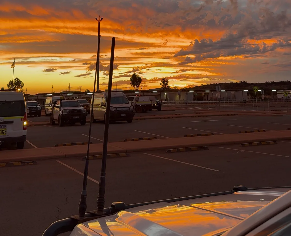 Parkplatz einer Mine in Westaustralien bei Sonnenuntergang, davor Pickups und ein Servicefahrzeug mit Funkantennen